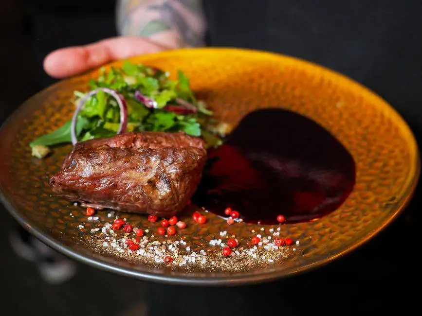 Delicious grilled steak served with leafy greens and rich sauce on a golden plate.