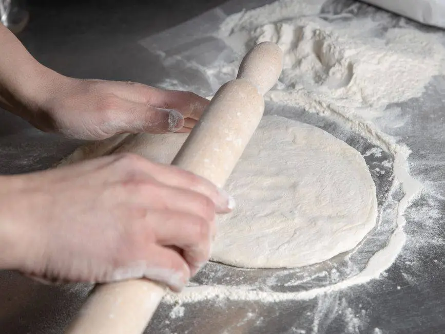 Close-up of hands rolling dough on floured surface, preparing for baking.