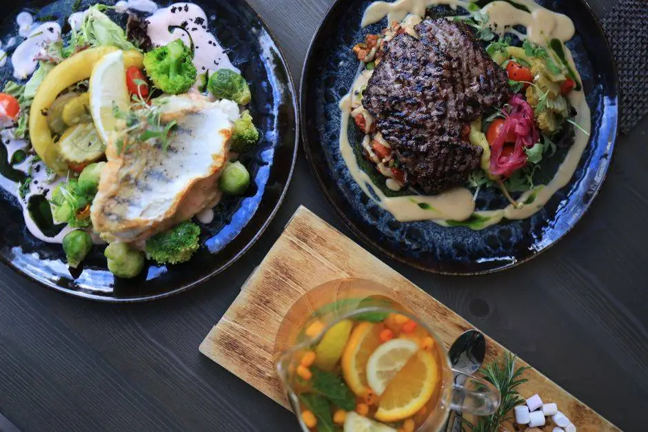 Top view of gourmet fish and steak dishes with fresh citrus and herbs on a stylish table setting.