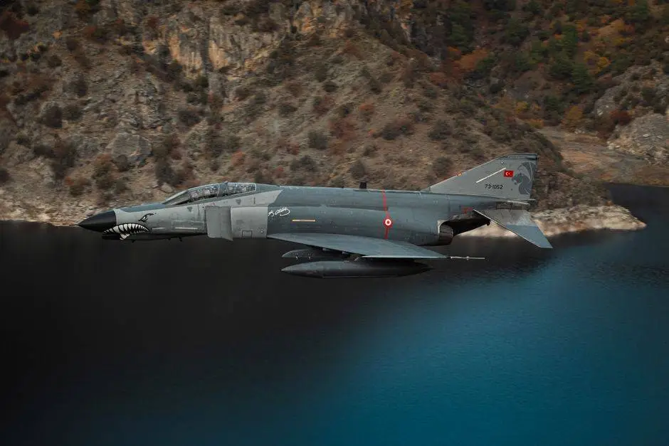 Turkish F-4 Phantom fighter jet flying over a scenic lake and cliffs in T&uuml;rkiye.