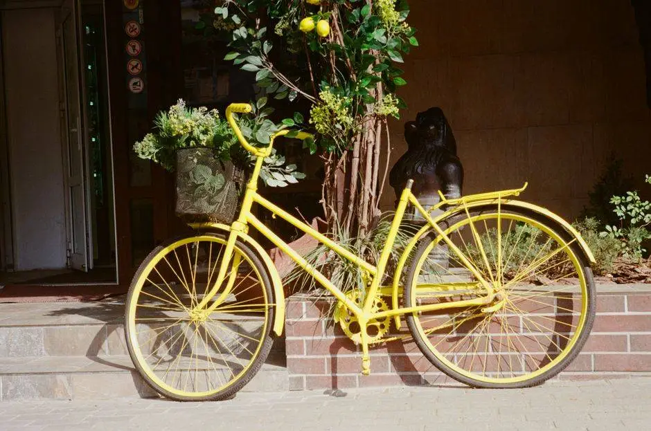 A vibrant yellow bicycle with a basket of lush plants parked on a sunny sidewalk.