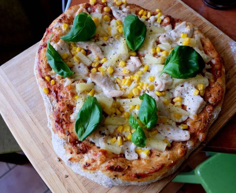 Delicious homemade chicken pizza topped with pineapples, corn, and fresh basil leaves.