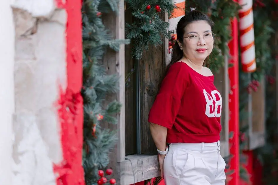 Woman in red top smiling by Christmas decorations, festive scene.
