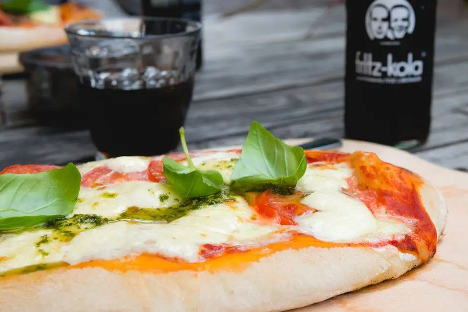 Close-up of a Margherita pizza topped with fresh basil and mozzarella, served with a glass of cola.