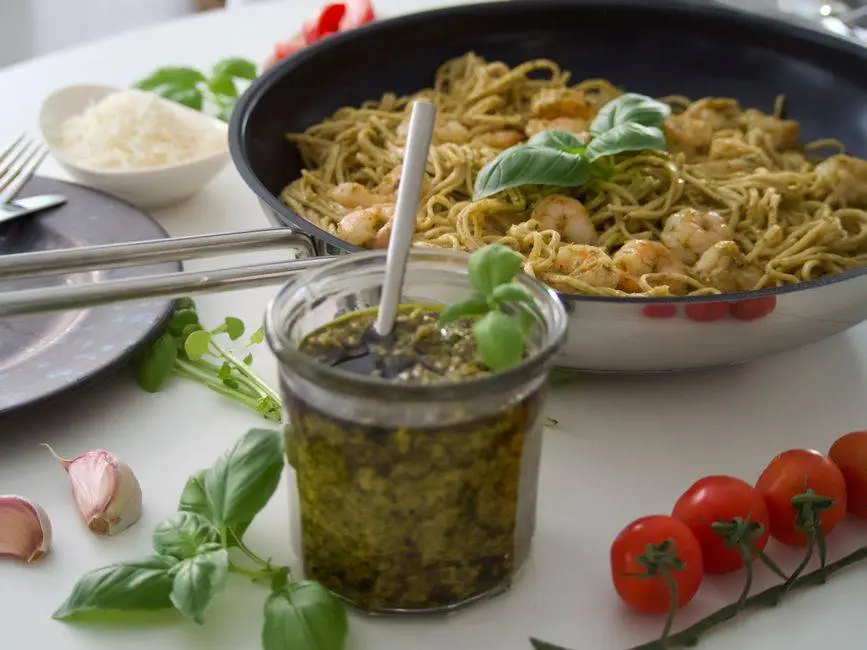 Delicious shrimp pesto pasta served with fresh basil, tomatoes, and parmesan cheese on a white background.
