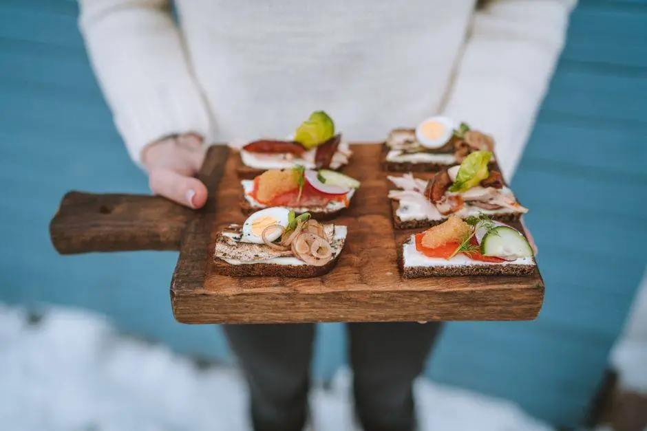 Close-up of open-faced sandwiches with eggs, vegetables, and meats on a wooden board.