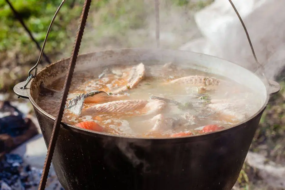 Ukha with assorted cooked fish pieces in cast iron pot with smoke diffusing in air on sunny day