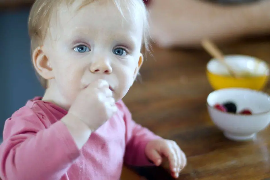 Close-up of a cute baby eating berries at a wooden table.